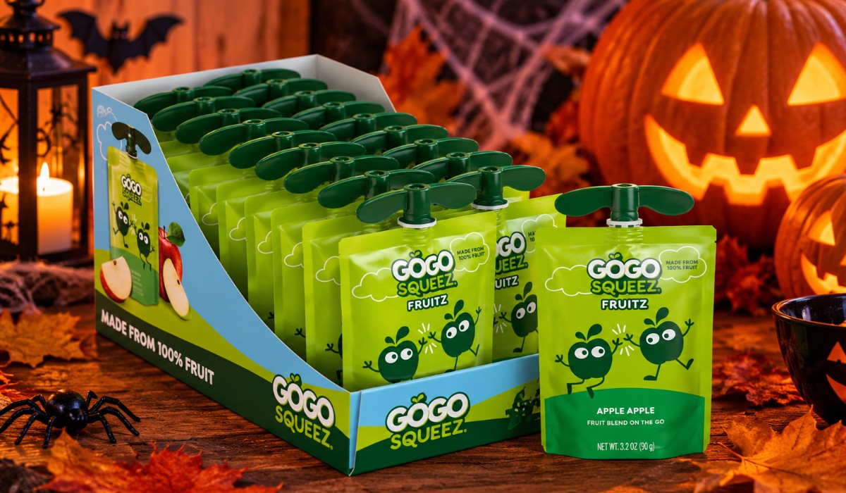 GoGo squeeZ apple fruit pouches in green packaging displayed on a wooden Halloween table with glowing pumpkins, autumn leaves and spooky decorations.